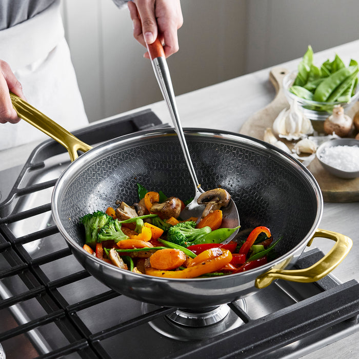 Vegetables being stir-fried in a gold ceramic-coated nonstick wok with fresh ingredients placed beside it.