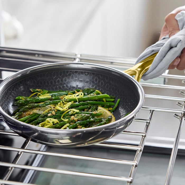Gold ceramic nonstick frypan with sautéed green beans and lemon slices, held in one hand.
