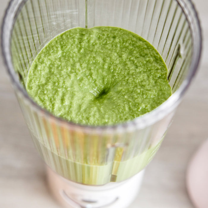 Cream portable blender filled with green smoothie, viewed from above on a light-colored surface.