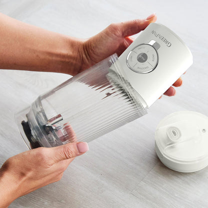 Person holding a white portable blender with GreenPan branding on a light gray surface.