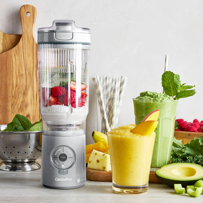 Blender with ingredients and two smoothies on a table