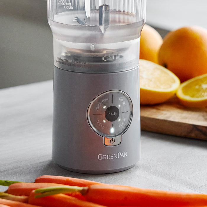 Gray blender with 'GreenPan' branding on a kitchen counter with fruits and vegetables.