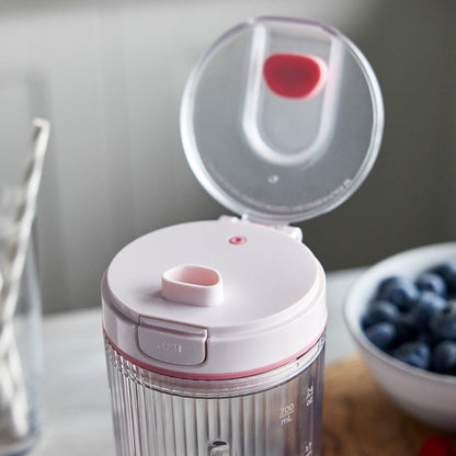 White and pink portable blender with a bowl of blueberries in the background