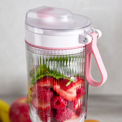 Pink portable blender filled with strawberries and raspberries on a light background
