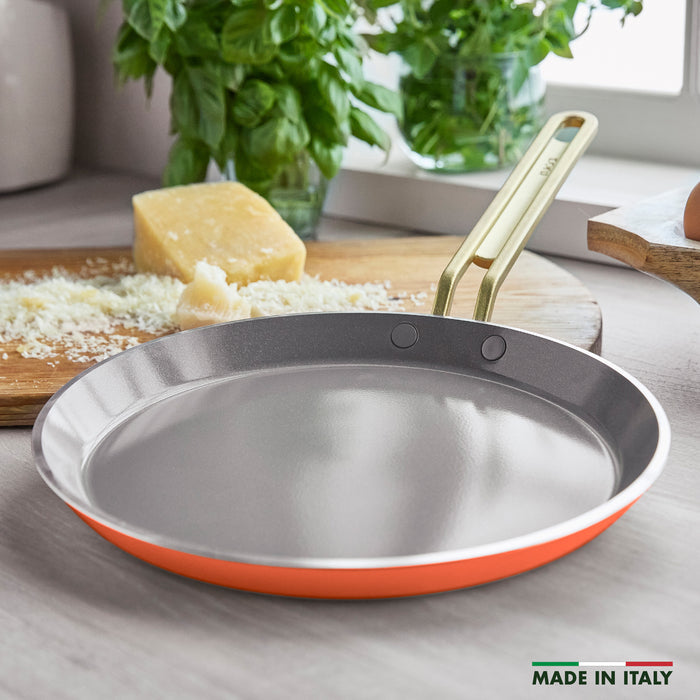 Gold-handled 10-inch pan sits on a counter next to grated cheese and fresh basil leaves.