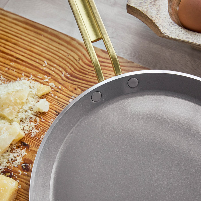 Copper-colored 10-inch pan with a gold handle next to grated cheese on a wooden board.