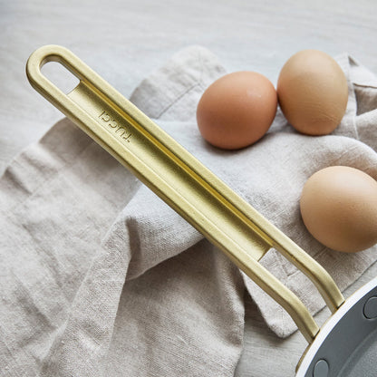 Gold crepe pan handle on a light gray towel with three brown eggs.