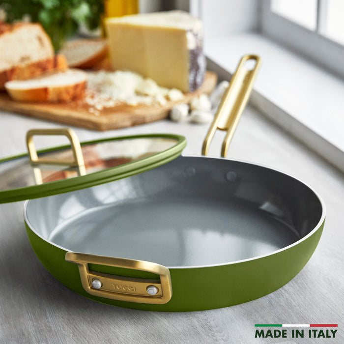 Ceramic nonstick 12-inch frypan with lid in green and gold handles, on a counter beside bread and cheese.