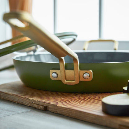 Stanley Tucci ceramic 12 frypan in green with gold handle, matching lid, and utensils visible in the background.
