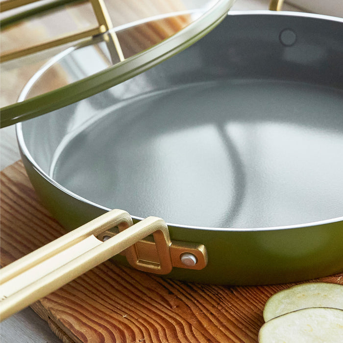 Olive green frypan with lid on a wooden board next to sliced eggplant.