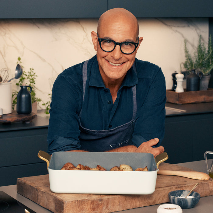 Man with glasses in kitchen stands behind roasted potatoes in a white Stanley Tucci™ ceramic lasagna pan.