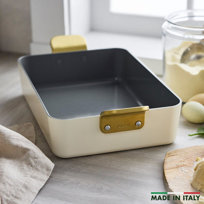Ceramic lasagna pan in white with gold handles on a kitchen counter.