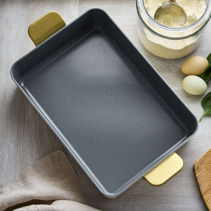 White ceramic lasagna pan with yellow handles, empty, on a kitchen table.
