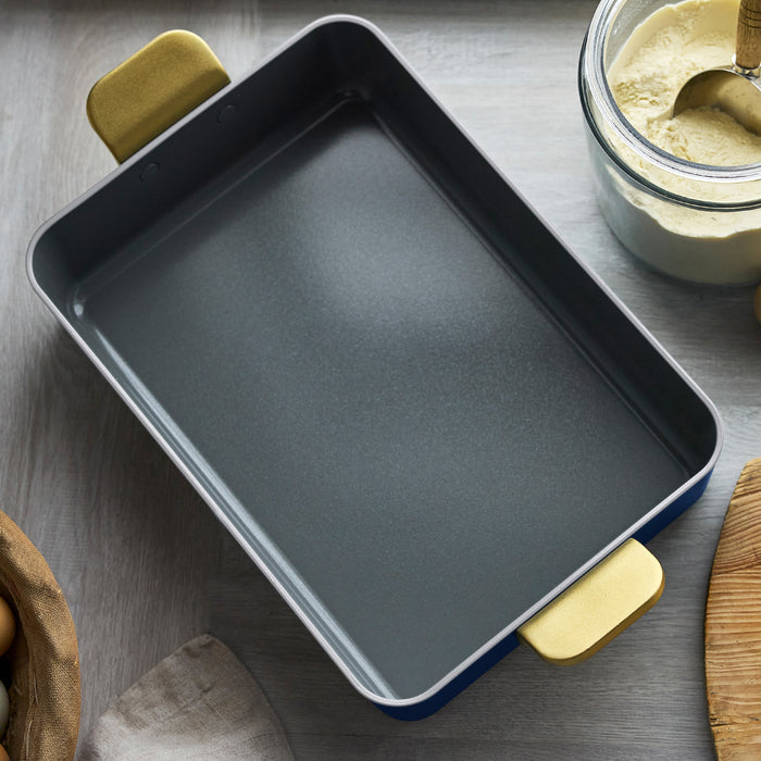 Ceramic lasagna pan in deep blue with yellow handles on a table near flour and a woven basket.