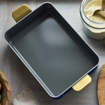 Ceramic lasagna pan in deep blue with yellow handles on a table near flour and a woven basket.