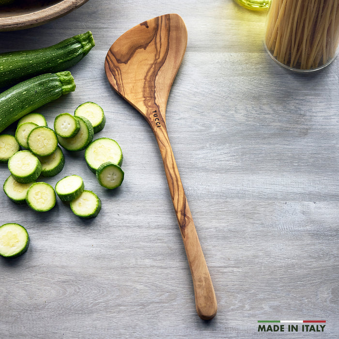 Wooden spoon with sliced zucchini on a gray surface