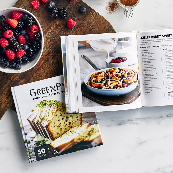 Berry-topped skillet rolls with fresh berries beside a closed copy of The Baking Cookbook on a table.
