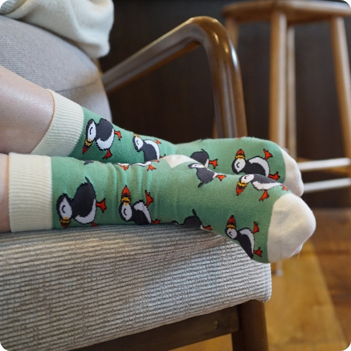 Person wearing green socks with puffin design sitting on a chair.