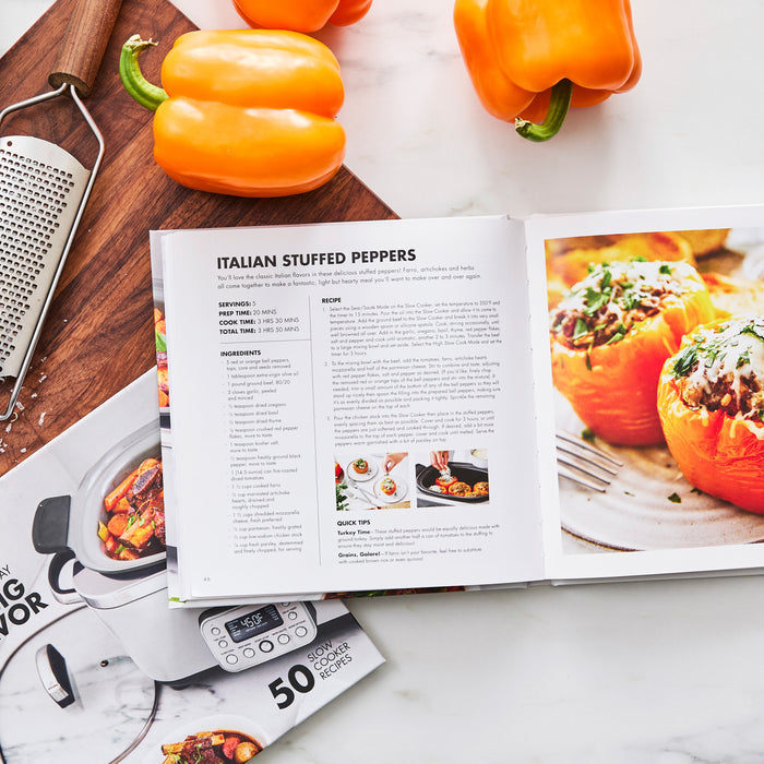 Open to an Italian stuffed peppers recipe, The Slow Way to Big Flavor Slow Cooker Cookbook, Vol. 2 sits on a kitchen counter with orange bell peppers, metal grater, cutting board, and part of the cookbook guide visible—ideal for meal prepping.