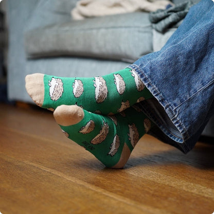 Green socks with hedgehog pattern worn by a person sitting on a wooden floor.