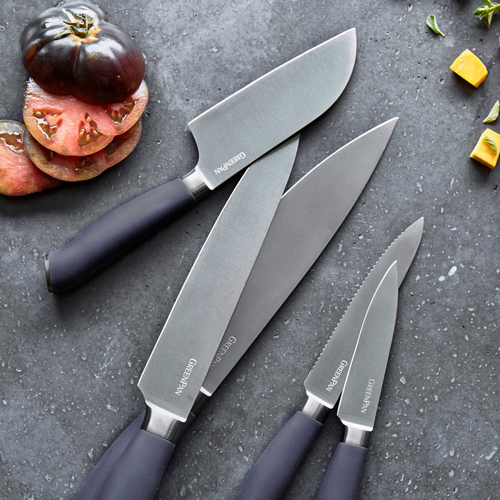 Titanium Santoku knife with three other kitchen knives on a gray counter, next to sliced tomatoes and vegetables.