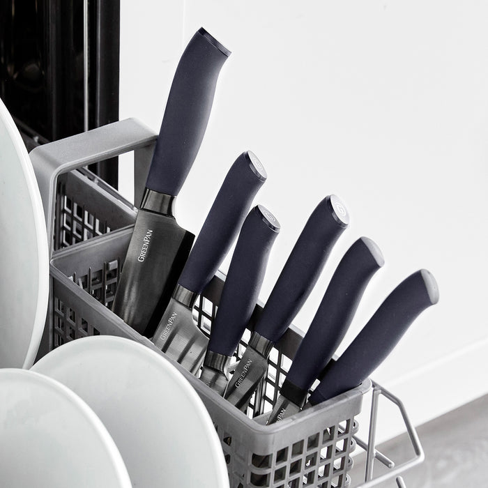 Santoku knife with black handle standing upright in a dishwasher basket beside white plates.