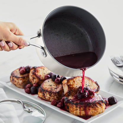 Hand pouring berry sauce from ceramic nonstick saucepan over grilled pork chops topped with whole berries.