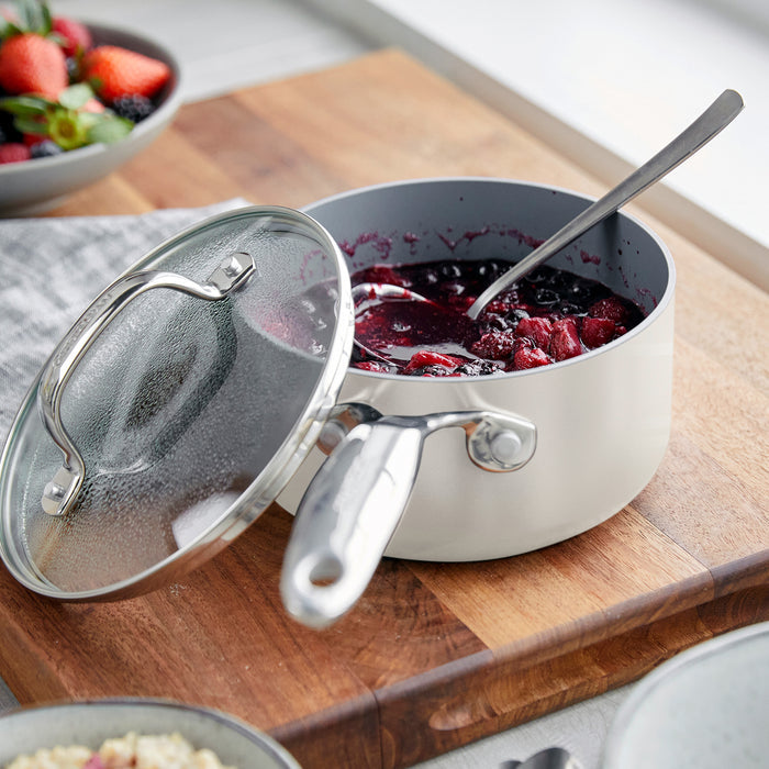 Cream ceramic nonstick saucepans, 1.5 and 3 qt sizes with lids, on a wooden board; one lid partly open.