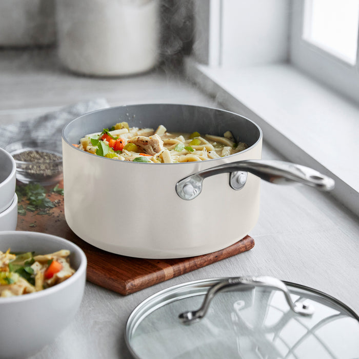Ceramic nonstick saucepan set with lids on a trivet by a window, bowls placed nearby.