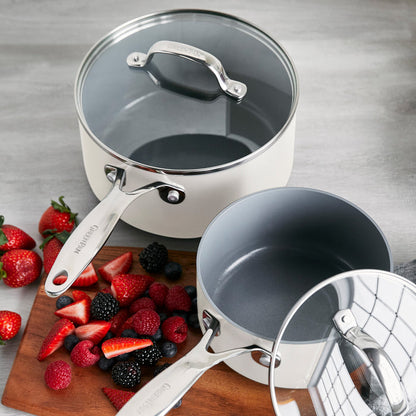 Two gray ceramic saucepans with lids next to a board of assorted fresh berries on a gray surface. Set includes two sizes.
