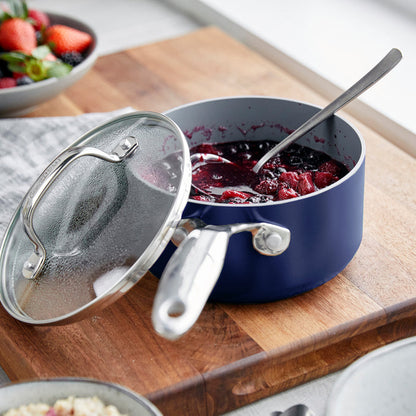 Two ceramic nonstick saucepans with lids in twilight blue, shown with berry compote and a spoon. Set includes 1.5-qt and 3-qt sizes.