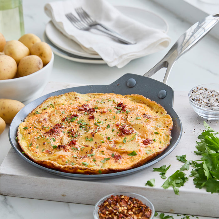 Golden potato frittata in a Valencia Pro 9.5-inch ceramic pan, served on white plates with herb garnish.
