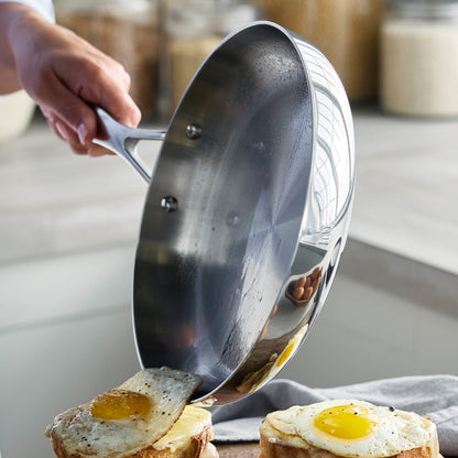 Stainless steel frypan with fried eggs being served onto bread on a kitchen counter.
