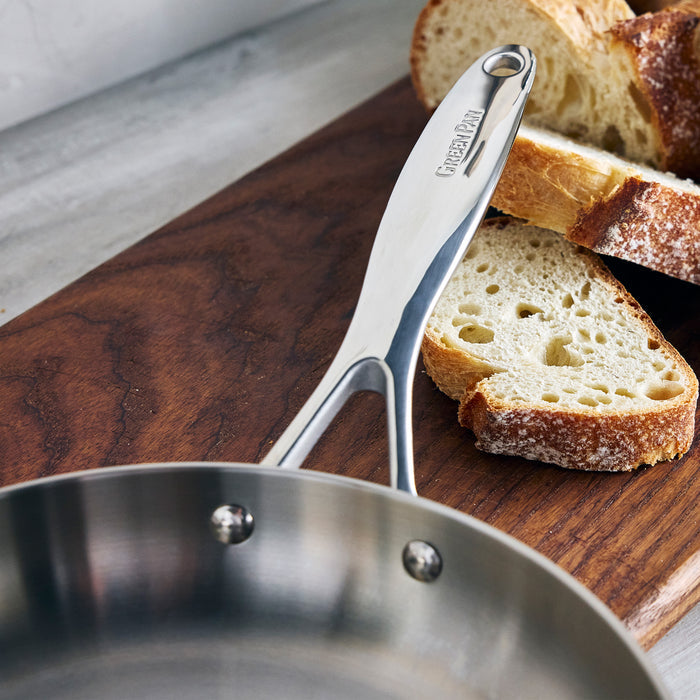 Stainless steel 12-inch frypan on a wooden board next to several slices of rustic bread.