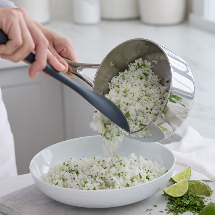 Stainless steel saucepan pouring herbed rice into a bowl, with lime wedges visible on the counter nearby.