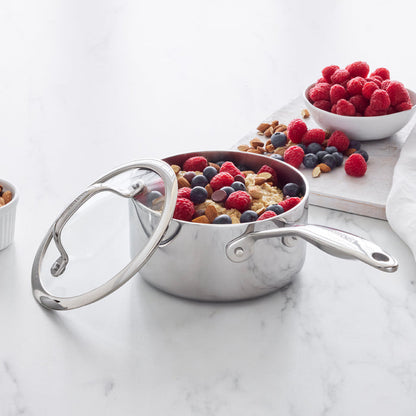 Stainless steel saucepan with oatmeal, berries, and nuts beside a small bowl of fresh raspberries.