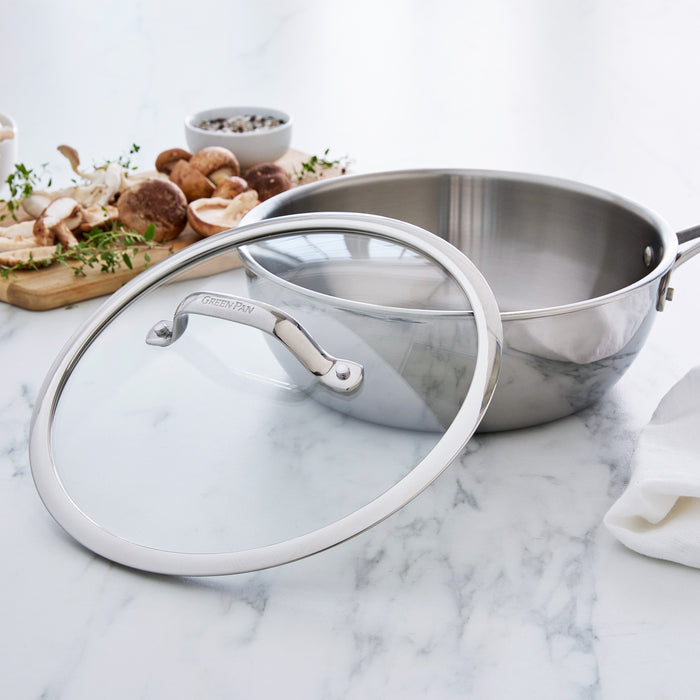 Stainless steel chef's pan set on a marble surface with ingredients in the background