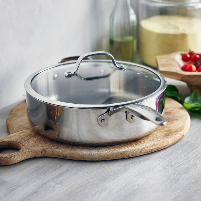 Stainless steel 5-quart sauté pan with lid on a wooden cutting board in a kitchen setting.