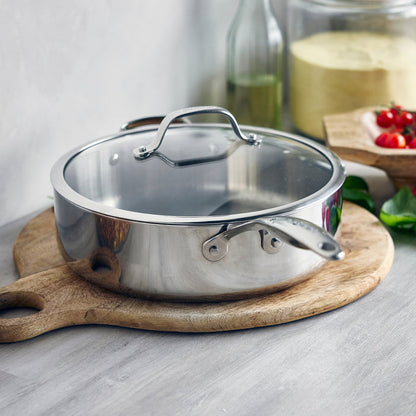 Stainless steel 5-quart sauté pan with lid on a wooden cutting board in a kitchen setting.